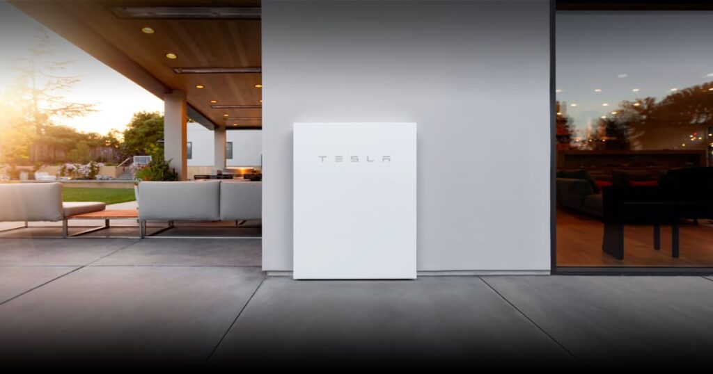 Een luxe woning met ruime tuin waar een Tesla thuisbatterij tegen de muur is geplaatst.