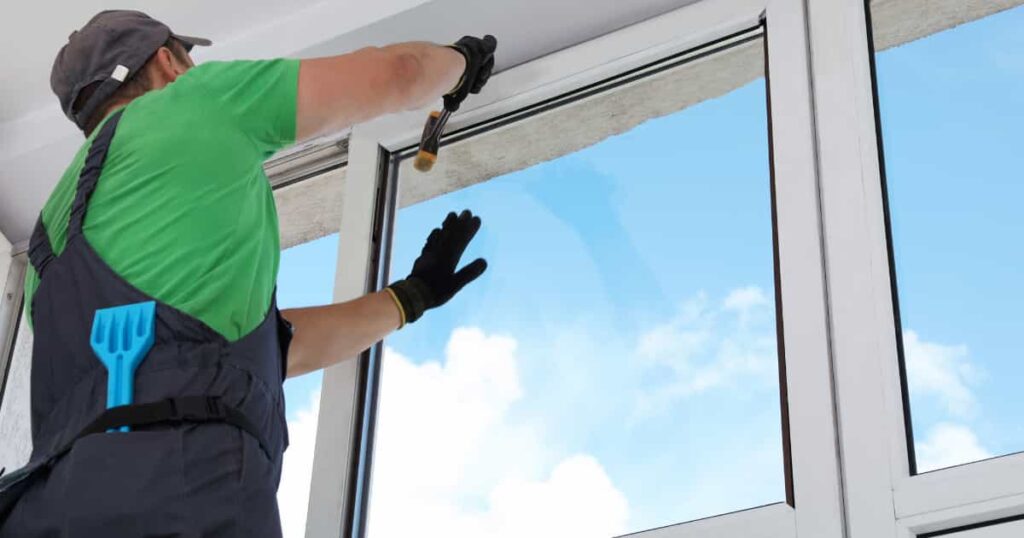 Een vakman dat nieuwe beglazing plaatst in een raam.