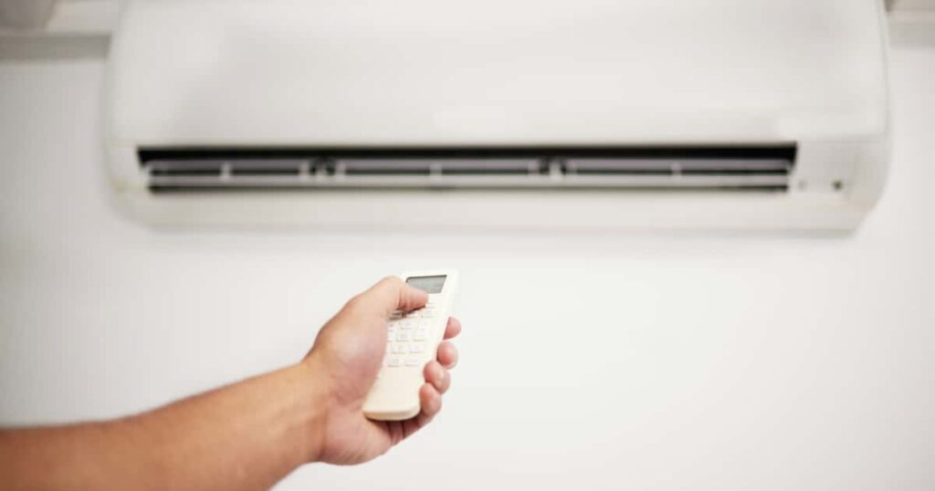 Een vaste airconditioning aan de muur en iemand dat met een afstandsbediening er naar wijst. 